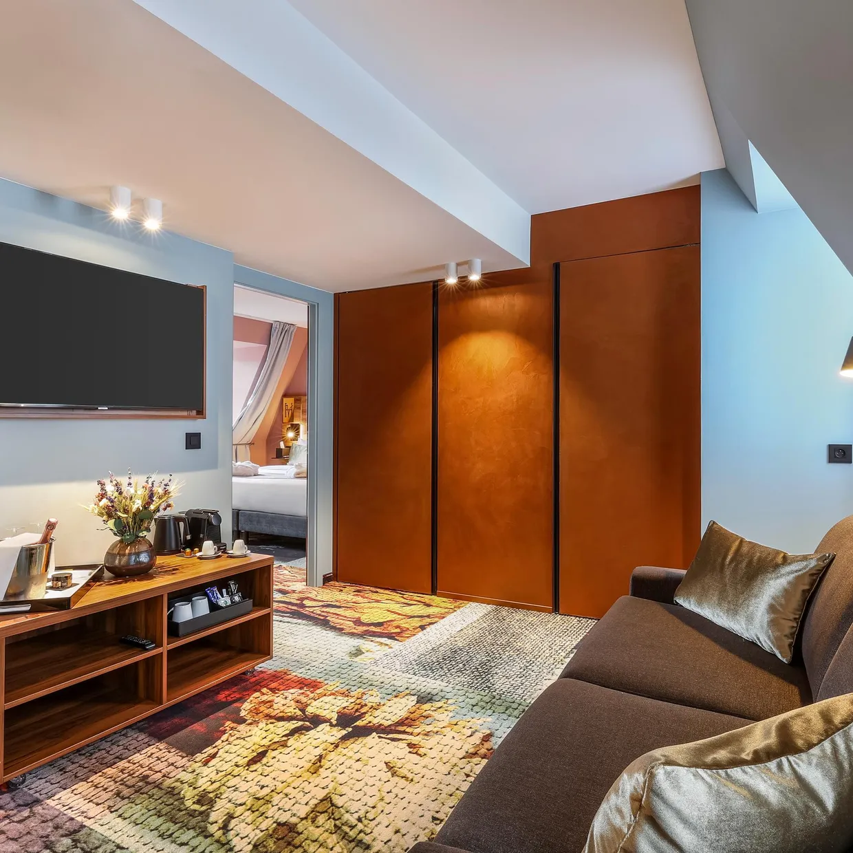 Hotelzimmer mit Sofa, Couchtisch, Fernseher und offener Tür zum Schlafzimmer