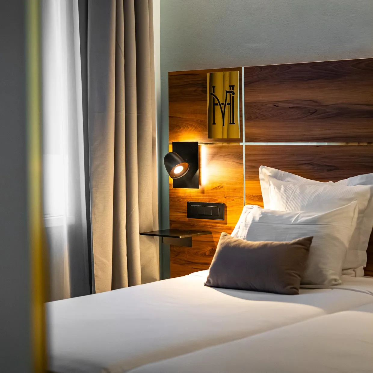 Bett mit Holz-Kopfteil, weißen Kissen und einem grauen Kissen, beleuchtet von einer Nachttischlampe