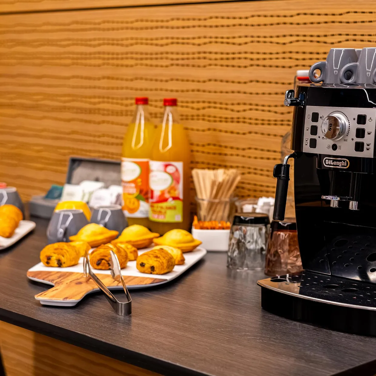 Tisch mit einer Kaffeemaschine, Tassen, Orangensaftflaschen, Orangen und Gebäck