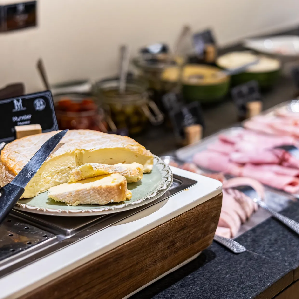 Ein Käsebrett mit einem Messer, Stücke von Hartkäse und Aufschnitt auf einem Buffettisch