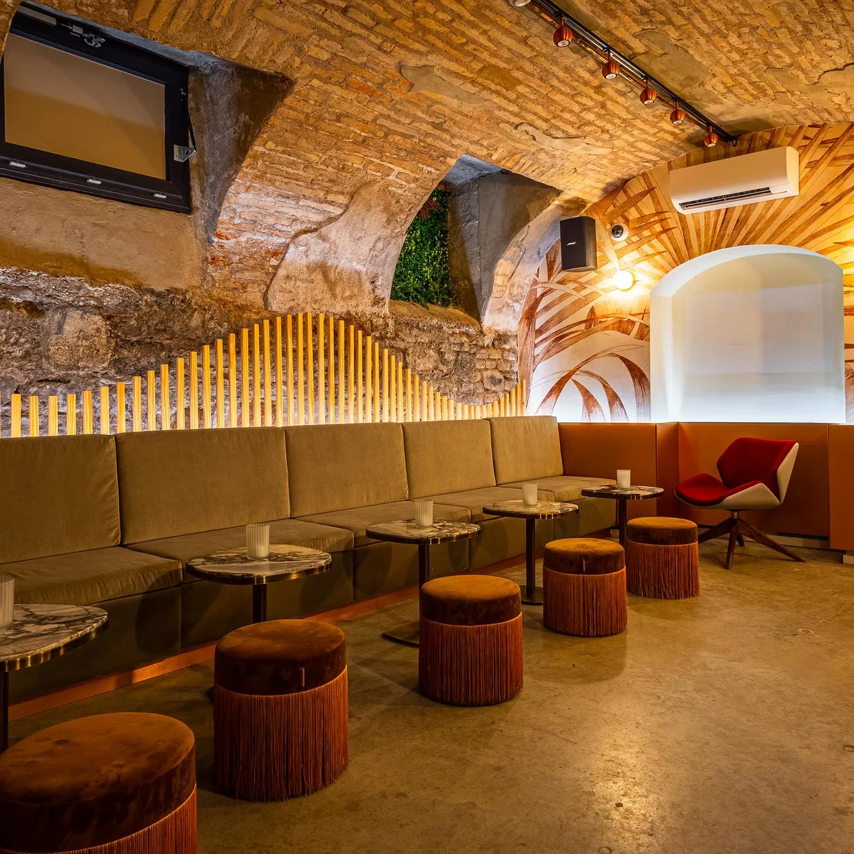 Ein Innenraum eines Bars oder Cafés, der in einem gewölbten Stein Keller eingerichtet ist, mit Ledersitzen, niedrigen Tischen und Holzhockern