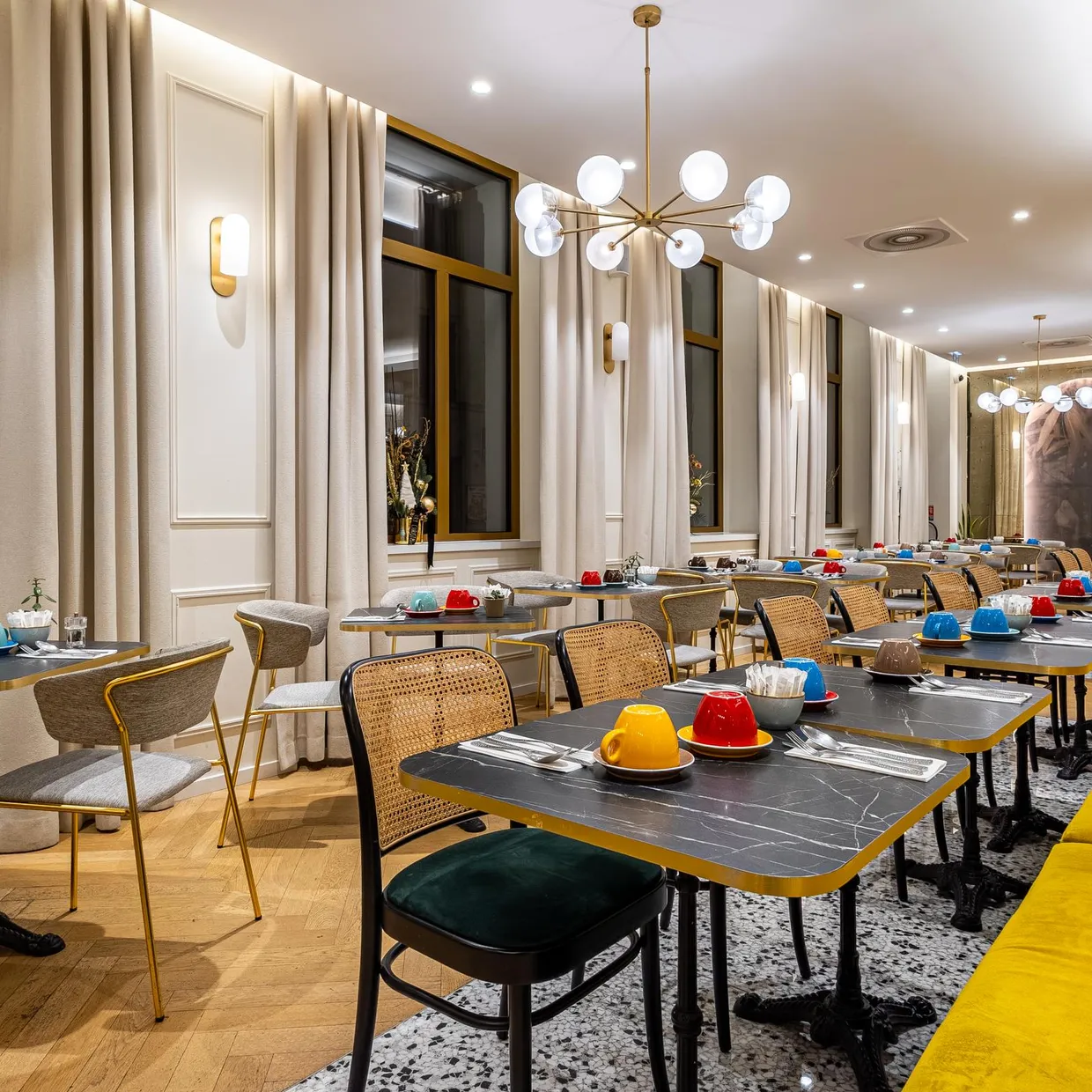 Ein elegantes Café mit runden Tischen, Stühlen und einem gelben Sofa, beleuchtet von modernen Hängelampen und Wandlampen