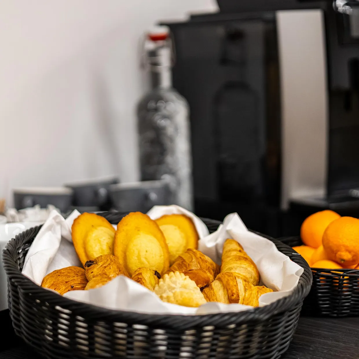 Ein Tablett mit Croissants, Orangen und Kaffeetassen vor einer Kaffeemaschine