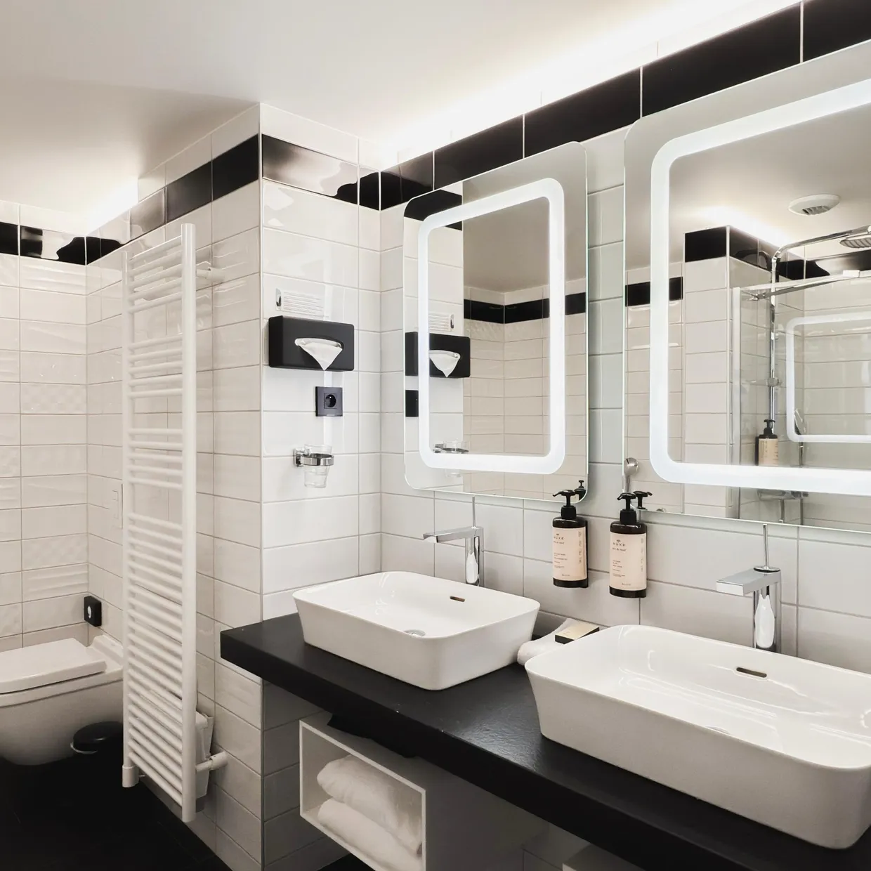 Moderne Badezimmer mit Toilette, Waschbecken, Badewanne, beleuchteten Spiegeln und aufgehängten Handtüchern
