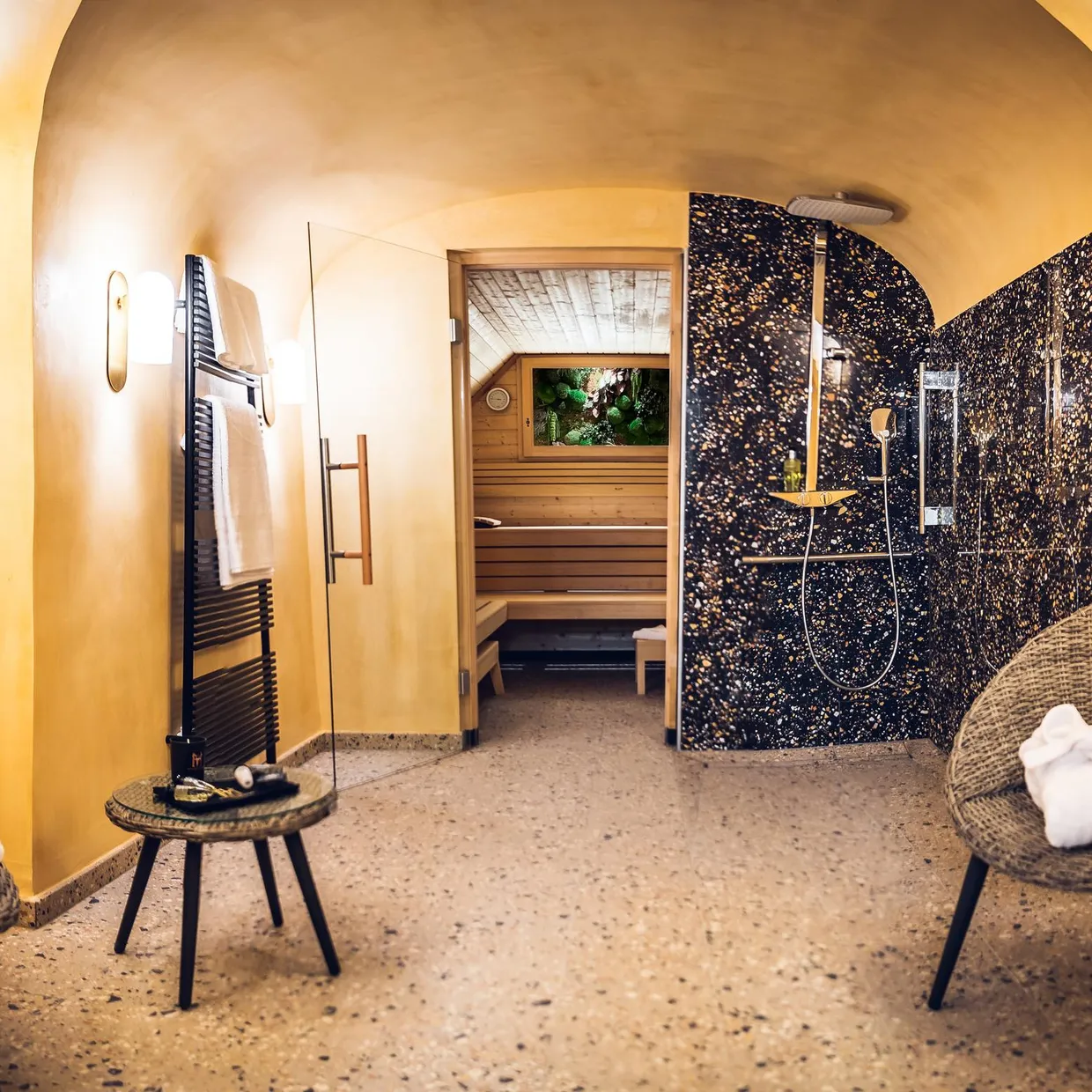 Spa-Raum mit zwei Korbstühlen, Handtüchern, einer Dusche und einem Zugang zu einer Holzzauna