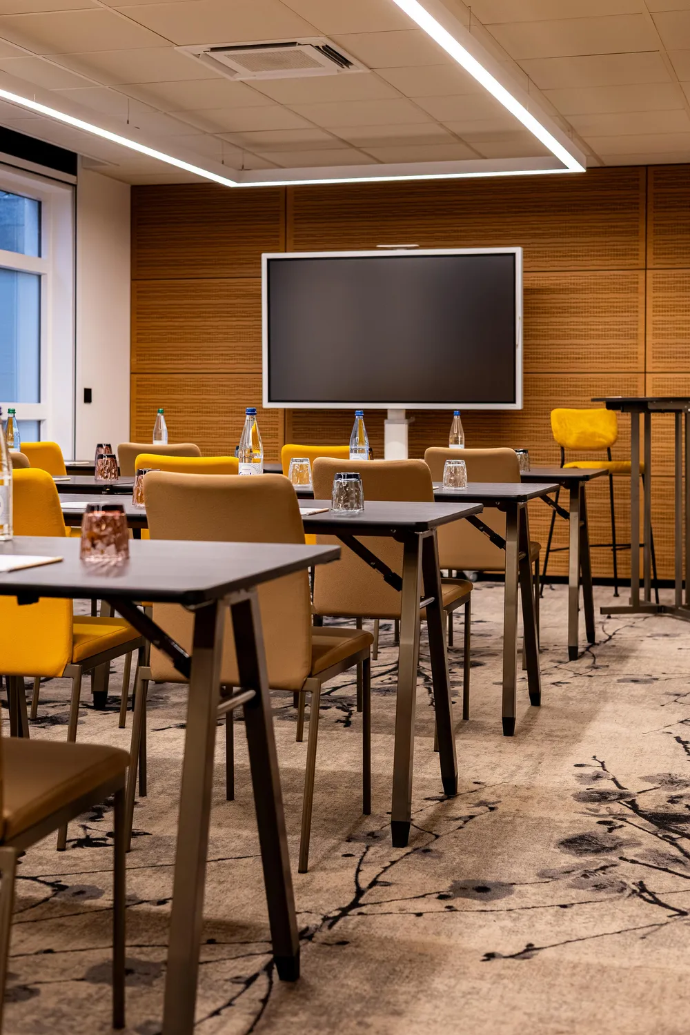 Meeting room with tables, chairs, water bottles, and a turned-off screen at the back