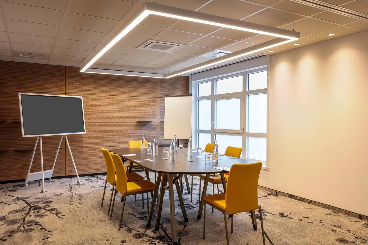 Meeting room with table, yellow chairs, screen and windows