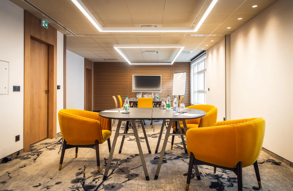 Meeting room with round table, yellow chairs, and screen at the back