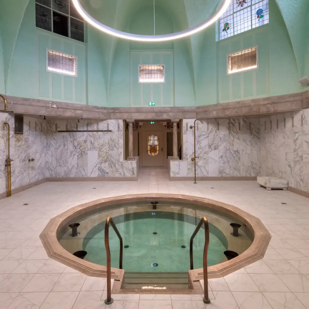 Une pièce circulaire avec une piscine centrale, des murs en marbre et un plafond voûté vert pâle éclairé