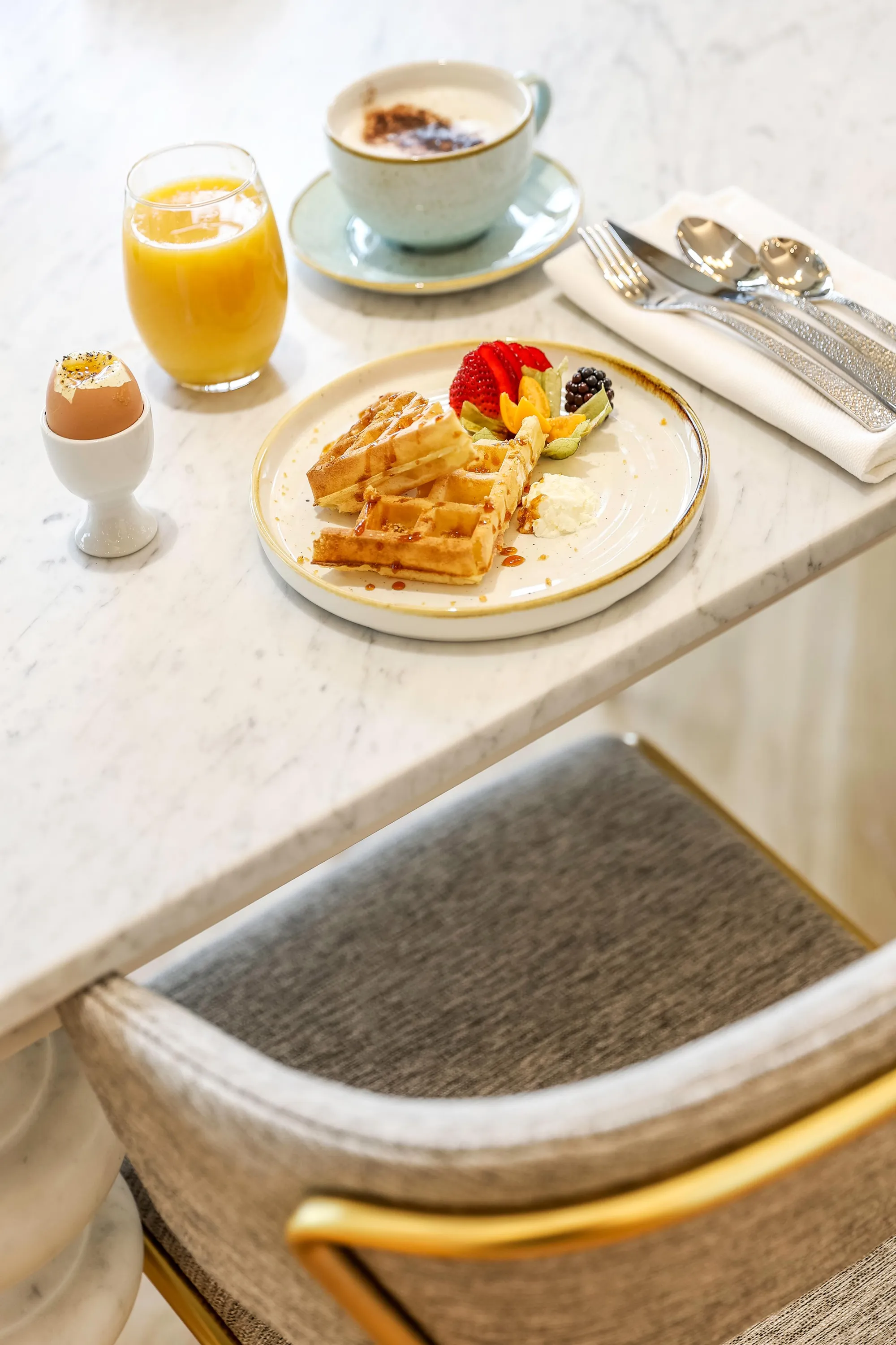 A breakfast tray with waffles, fruit, a soft-boiled egg, a glass of orange juice, and a cup of coffee.