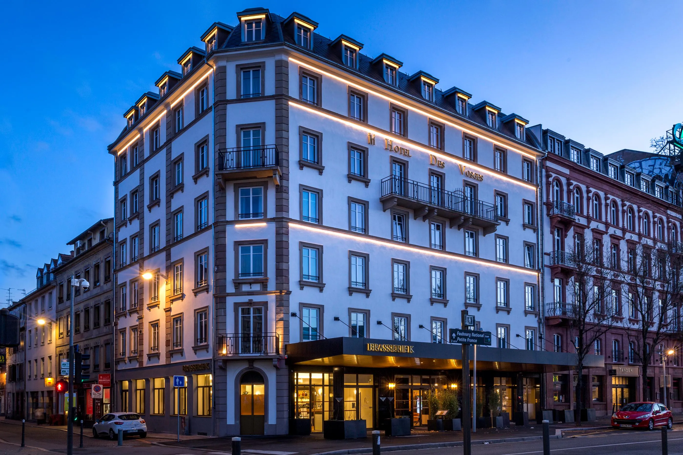 Eckgebäude nachts beleuchtet mit der Aufschrift "Hotel Des Voyageurs" und einem Restaurant im Erdgeschoss