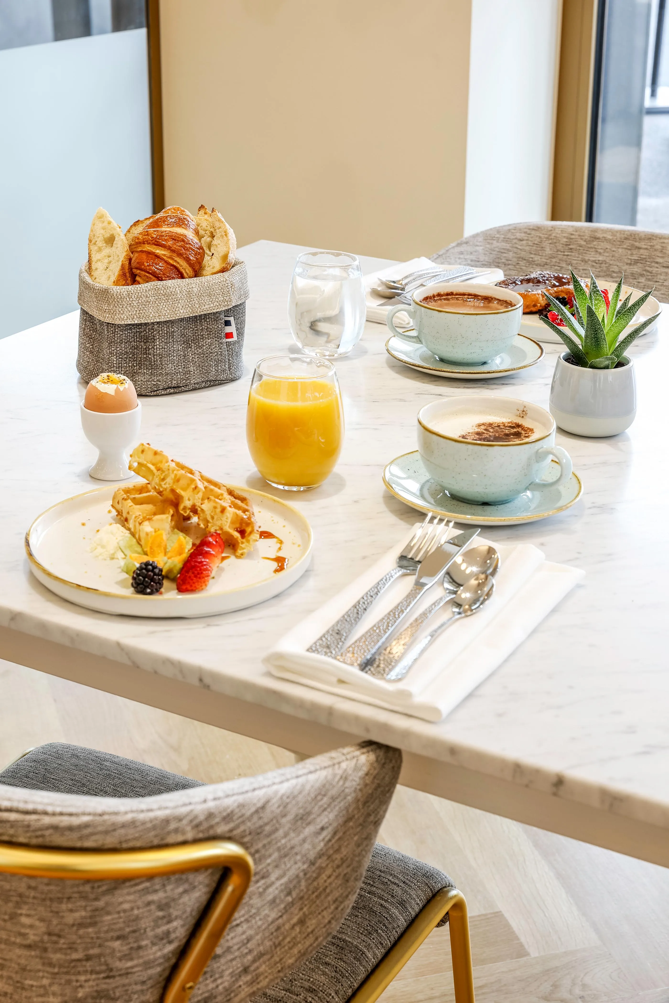 Tisch mit Frühstück bestehend aus Croissants, Eiern, Waffeln, Orangensaft, Kaffee und Obst