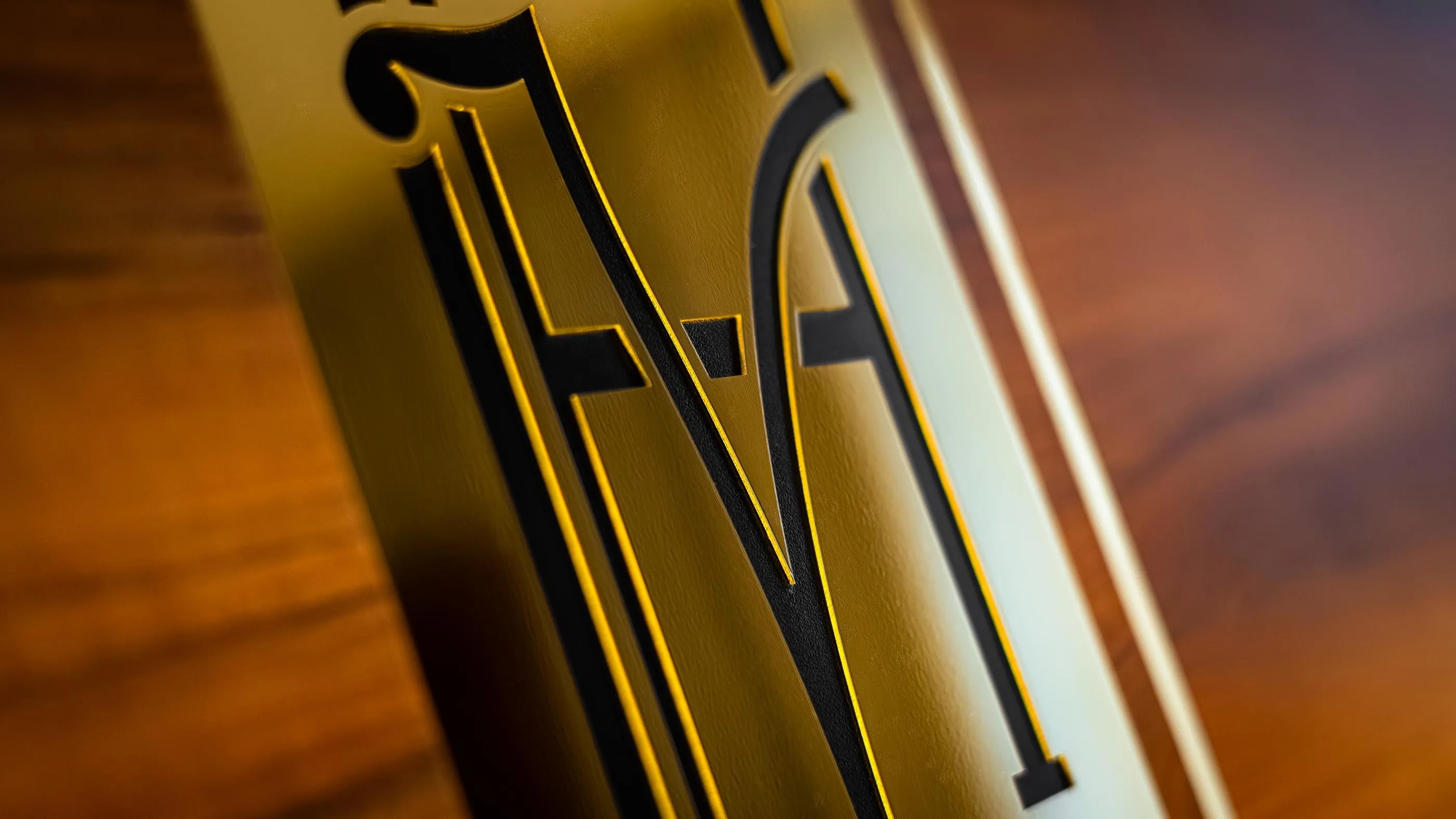 Detail einer vergoldeten Platte mit den erhabenen Buchstaben "MA" auf braunem Untergrund