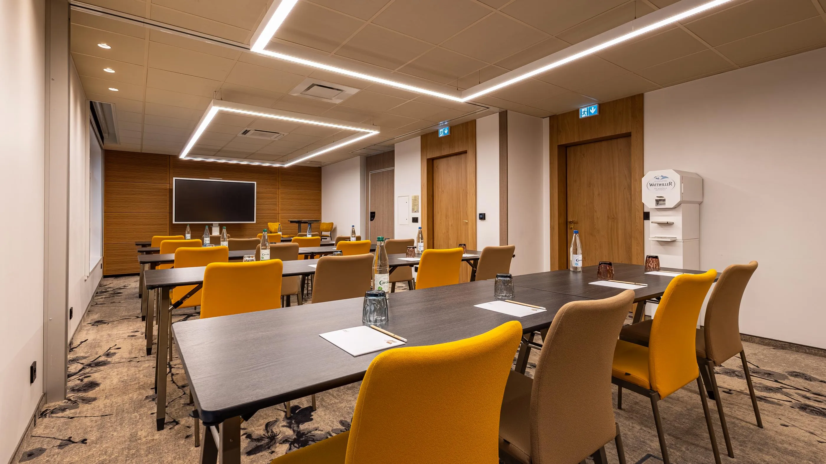 Meeting room with tables and chairs, screen at the back, water dispenser and bottles on the tables