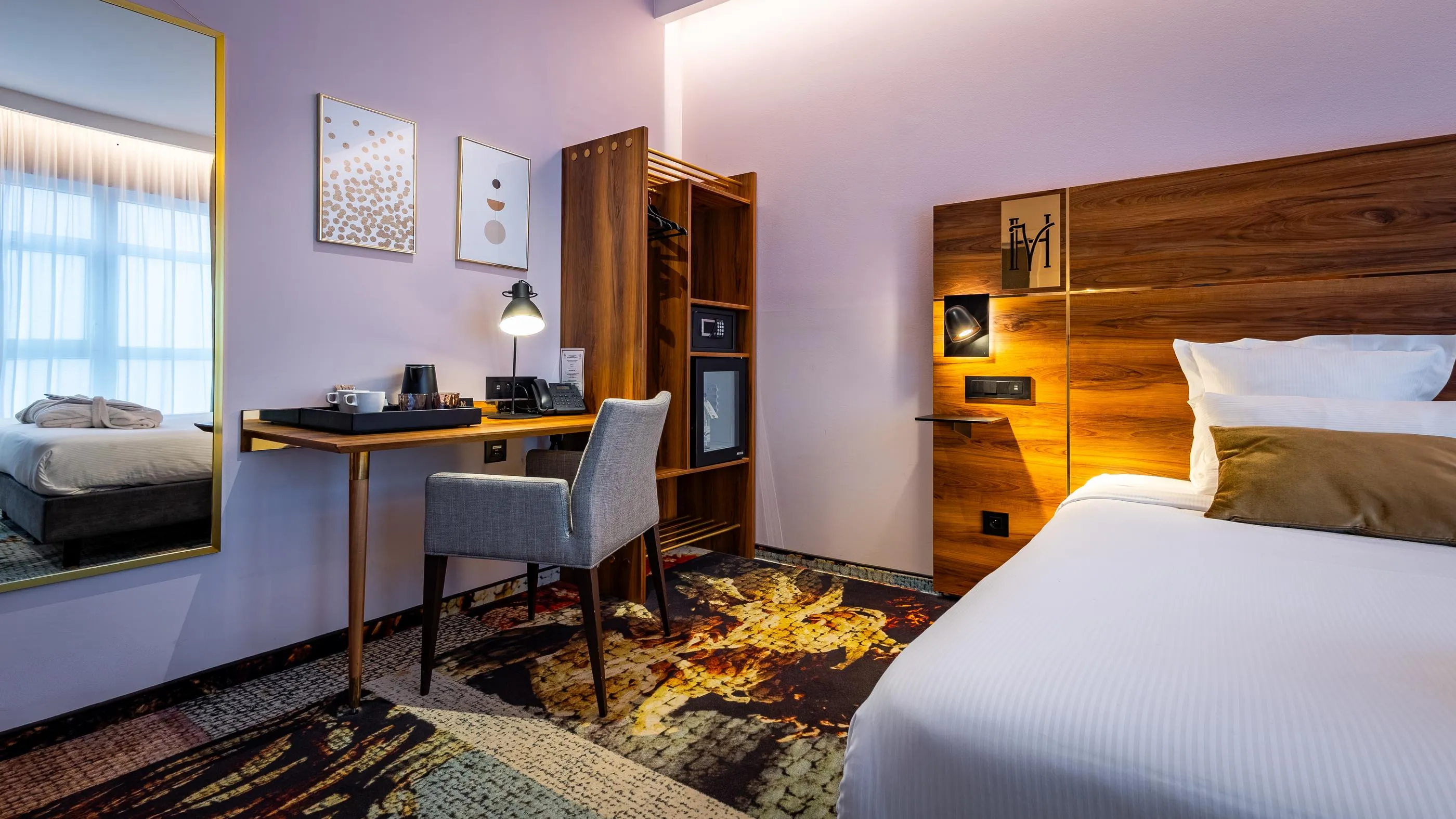 Hotelzimmer mit zwei Betten, einem Schreibtisch, einem Stuhl und einem Holzschrank, beleuchtet durch ein Fenster und Wandlampen