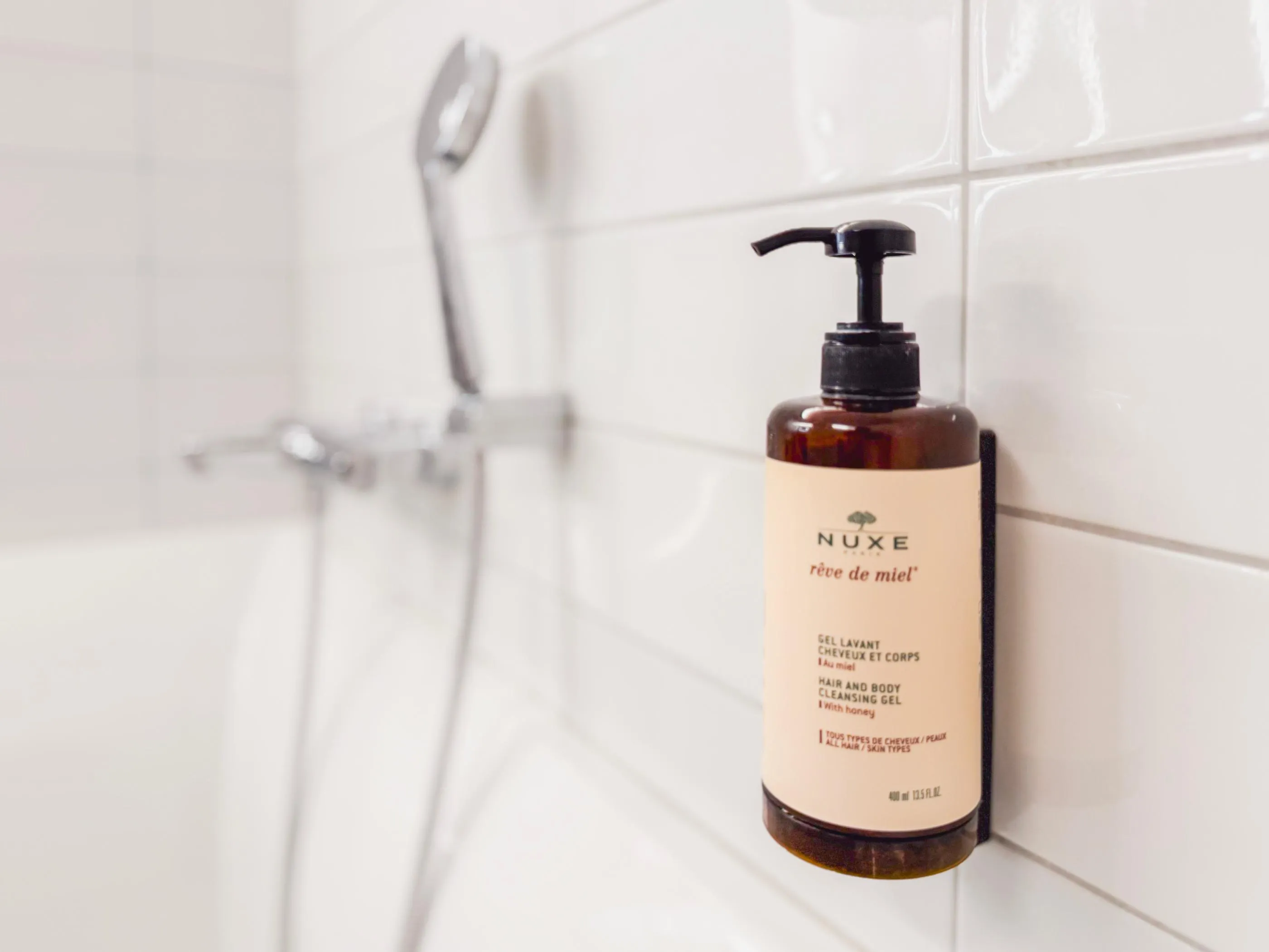 Nuxe "rêve de miel" shampoo bottle fixed to a tiled wall near a shower head