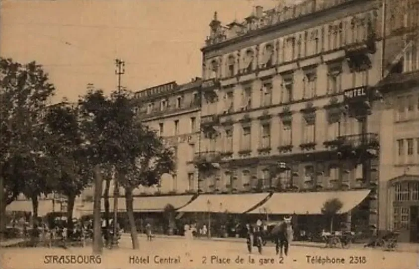 Alte Schwarz-Weiß-Fotografie eines mehrstöckigen Gebäudes mit Balkonen, Bäumen und Passanten davor in Straßburg, mit einem Schild "Hôtel Central" sichtbar
