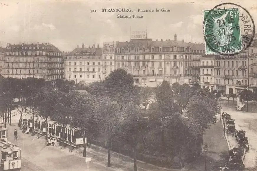 Bahnhofplatz in Straßburg mit historischen Gebäuden, Bäumen und fahrenden Straßenbahnen