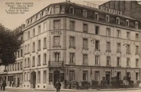 Altes Gebäude des Hôtel des Vosges mit einer Person, die davor geht, geparkten Fahrzeugen und sichtbaren Schildern an der Fassade