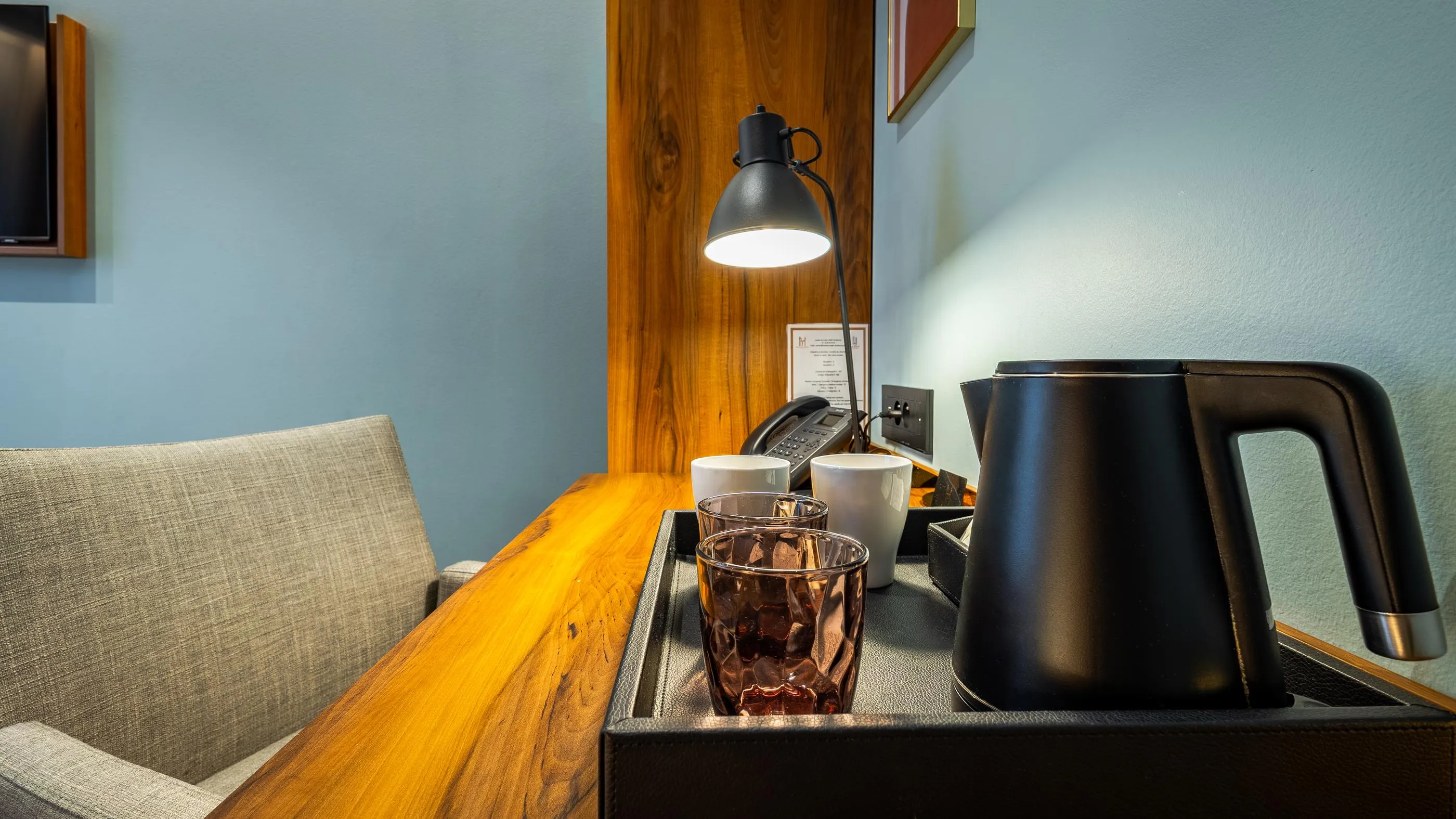 Ein Wohnbereich mit einem Holztisch, einer eingeschalteten Lampe, einem Wasserkocher, Gläsern und einem Telefon