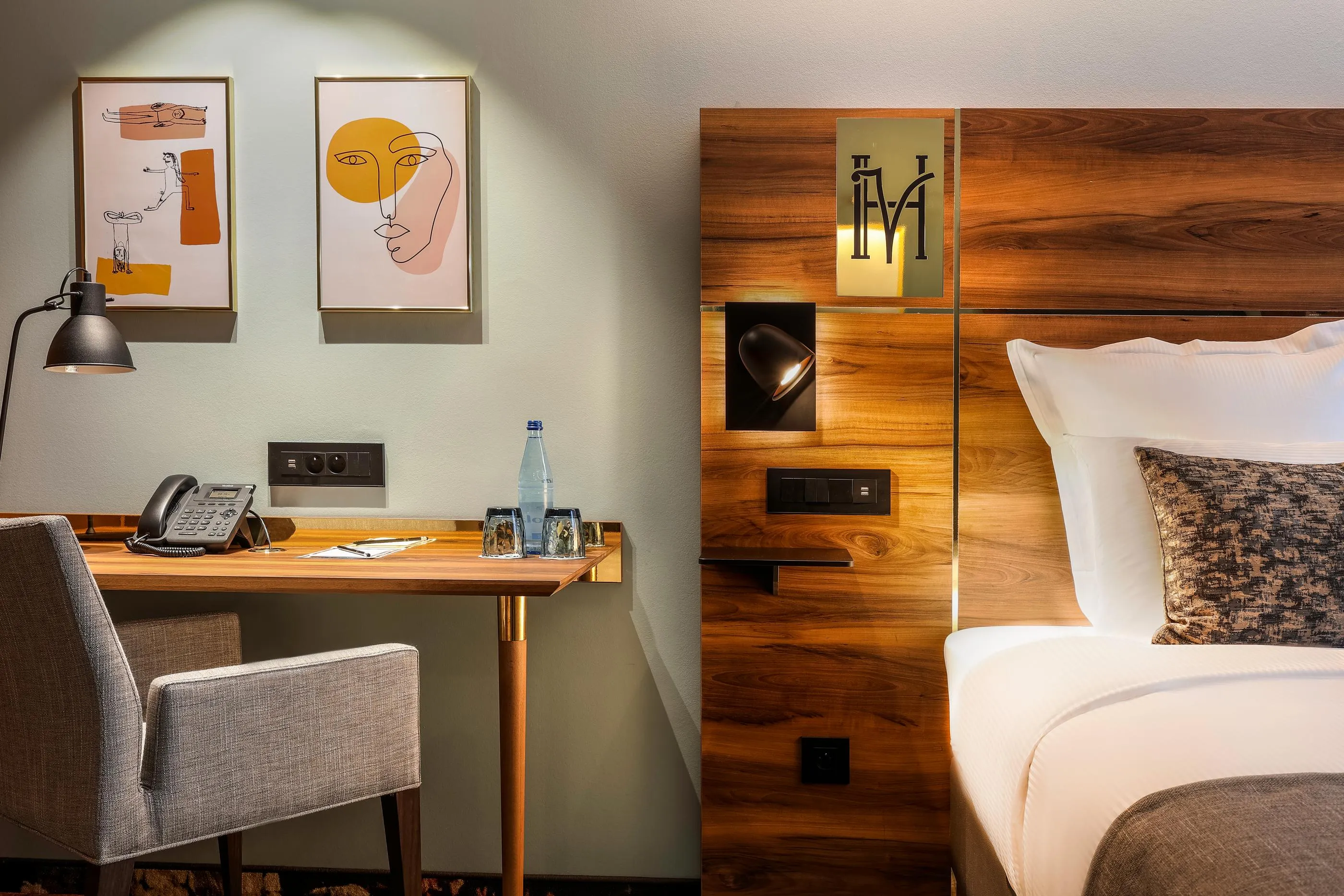 Hotel room with a desk, a chair, a telephone, a water bottle, and a bed with pillows