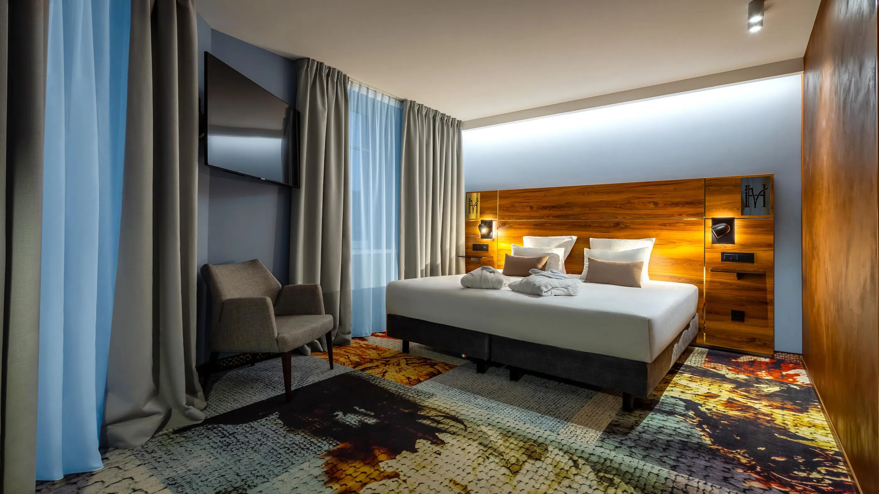 Hotel room with a double bed, two armchairs, a wooden headboard, and gray curtains