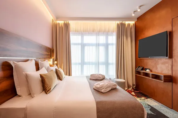 Hotelzimmer mit einem Doppelbett, Kissen, einem Flachbildfernseher und einem großen Fenster mit Vorhängen