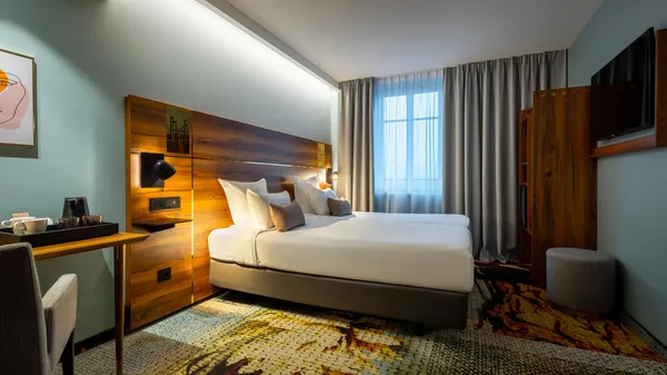Hotelzimmer mit einem Doppelbett, einem Schreibtisch, Vorhängen und einer Wanddekoration