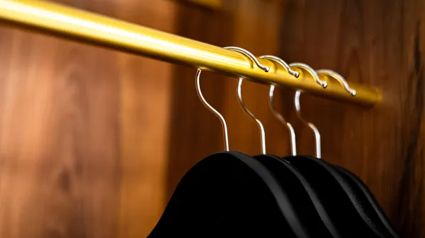 Metal hangers attached to a gold-colored rod in a wooden wardrobe