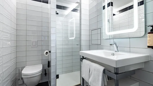 Modern bathroom with toilet, sink, illuminated mirror, and white-tiled shower