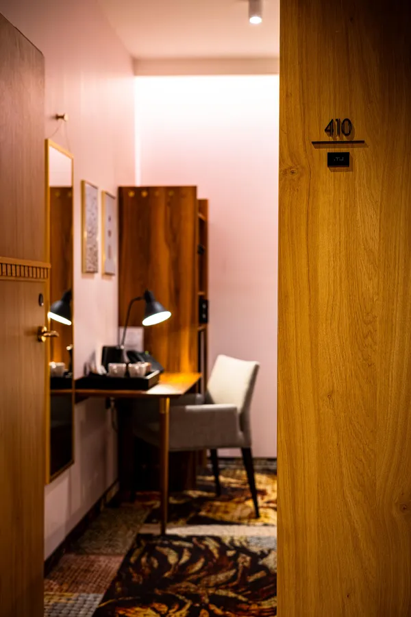 View of a hotel room with a desk, a lamp, and a chair, seen from the hallway with door number 410 open