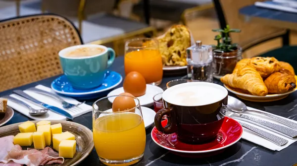 Table de petit-déjeuner avec café, jus d'orange, croissants, œufs, beurre, charcuterie et couverts
