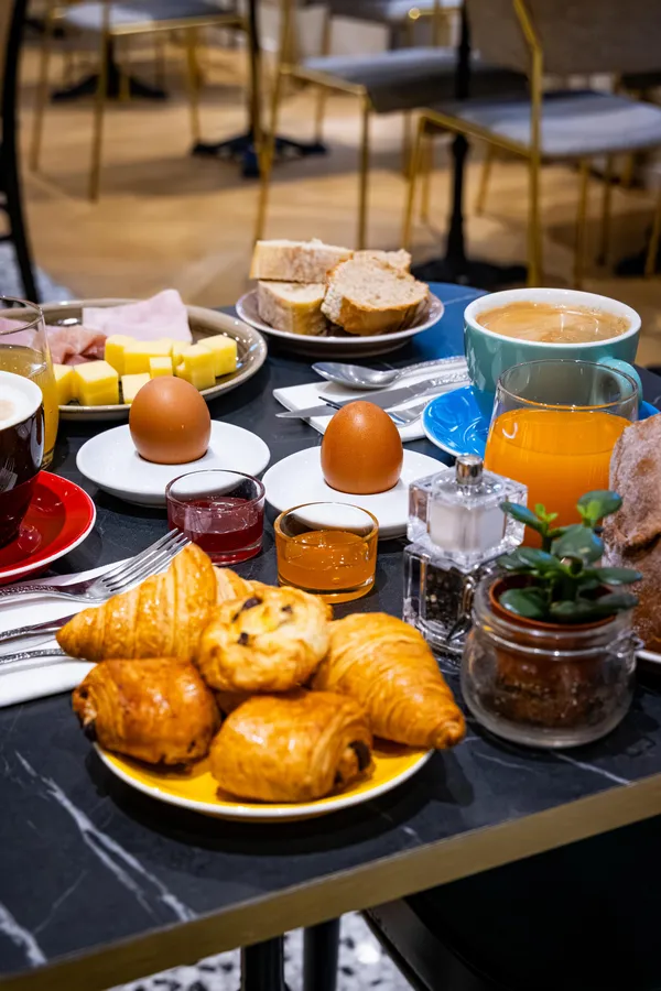 Table set with croissants, eggs, bread, orange juice, coffee, and other breakfast foods