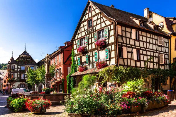 Place de village avec des maisons à colombages, des fleurs et une fontaine
